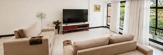Sala da cobertura linear no Jardim Oceânico, com sofás bege, TV e porta de vidro para o terraço