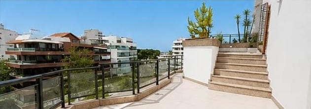 Terraço da cobertura linear no Jardim Oceânico, com guarda-corpo de vidro, escada de pedra e vista para os prédios e o mar