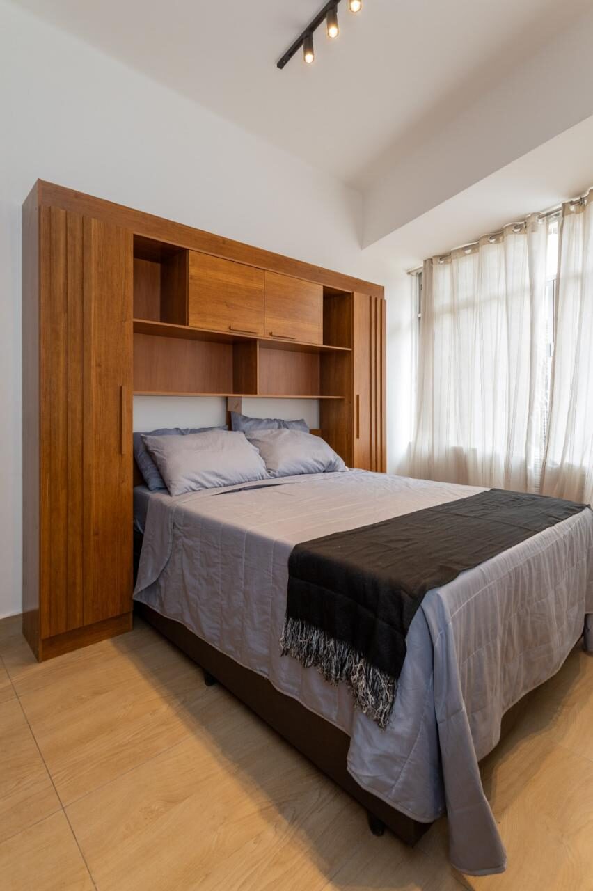 Cama de casal do estúdio em Copacabana, com cabeceira de madeira e nichos embutidos