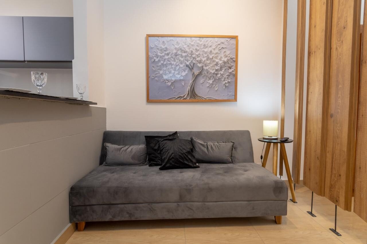 Sala do estúdio em Copacabana, com sofá cinza, quadro de árvore e divisória de ripas de madeira