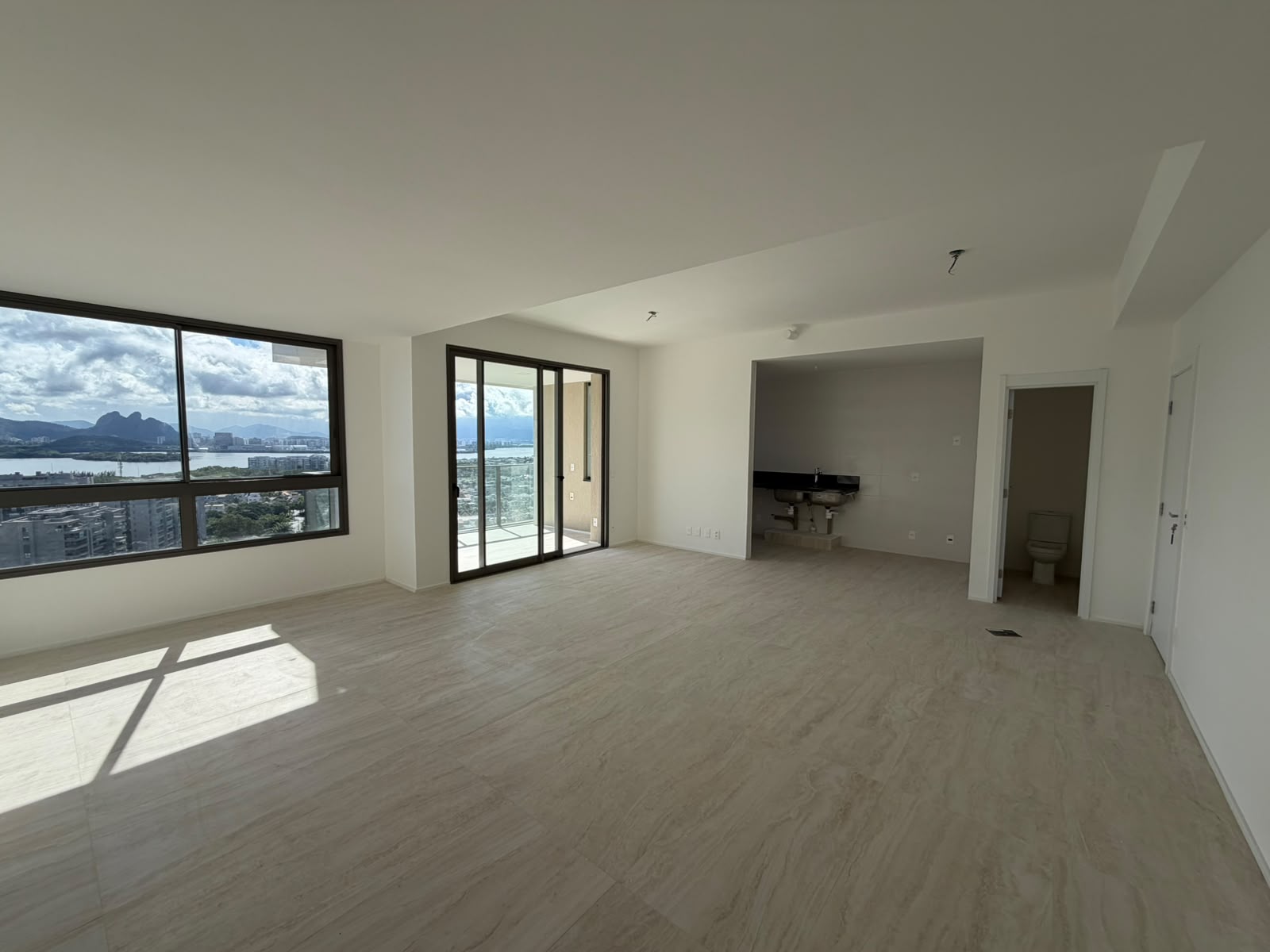 Sala ampla vazia do apartamento em Copacabana, Posto 4, com piso claro, varanda com porta de vidro e vista para a lagoa e morros