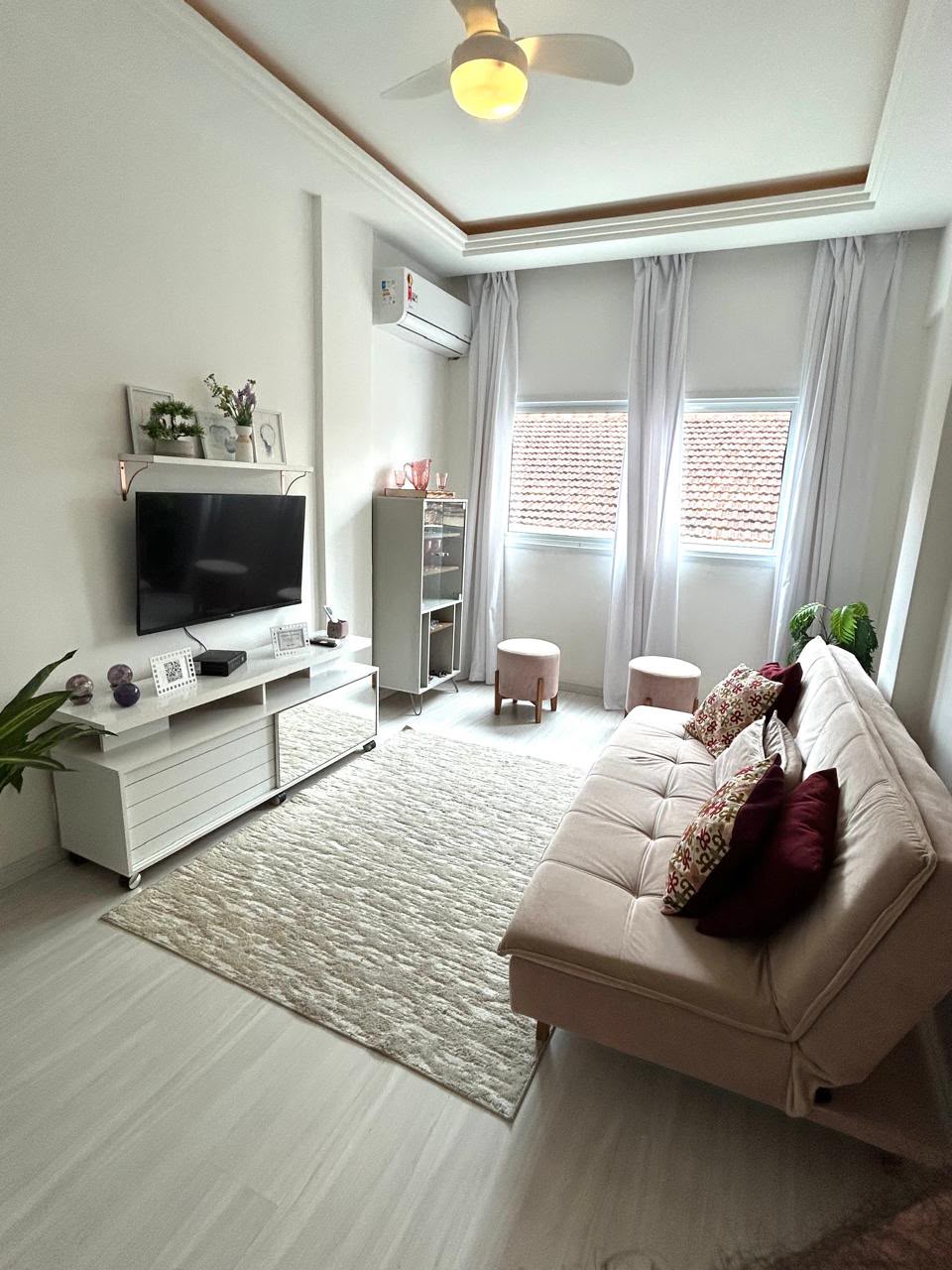 Sala de estar clara e decorada do apartamento em Copacabana, Posto 4, com sofá retrátil bege, painel de TV branco e ar-condicionado