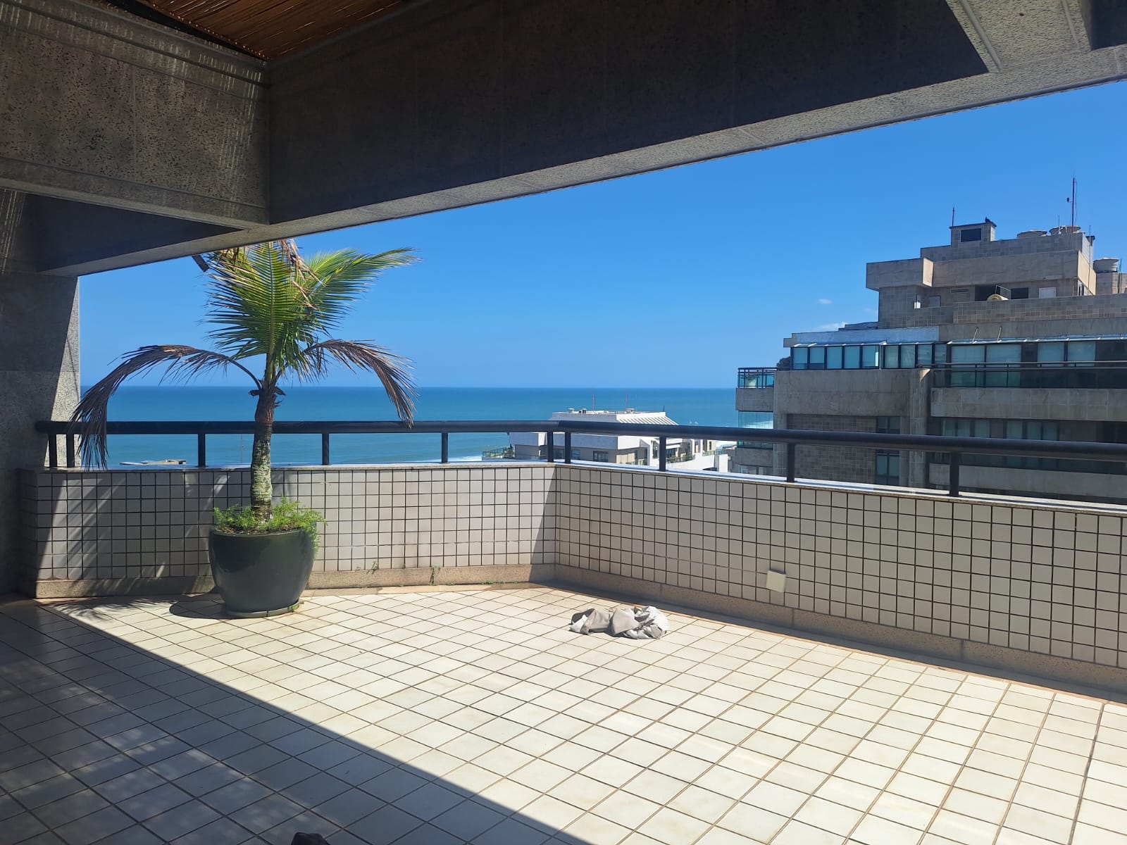 Varanda da cobertura dúplex Golden Green, na Barra da Tijuca, com piso de azulejos claros, vaso de palmeira e vista para o mar