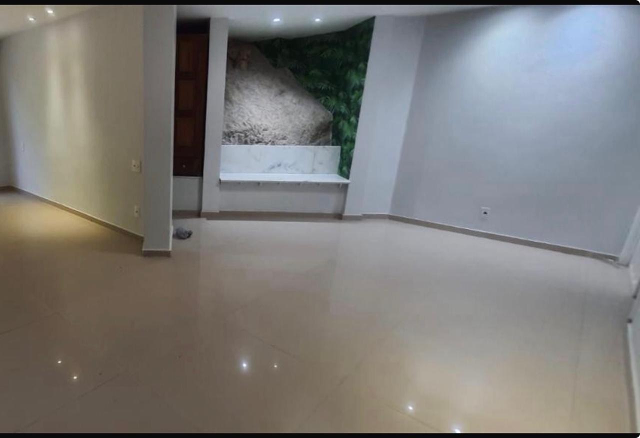 Sala ampla e vazia do apartamento para locação em Ipanema, com piso porcelanato claro, bancada de mármore e painel de folhagens ao fundo