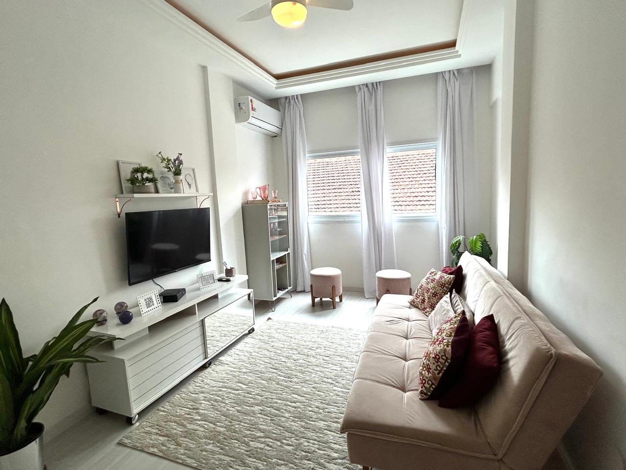 Sala do apartamento em Ipanema vista da entrada, com sofá bege, TV e ar-condicionado