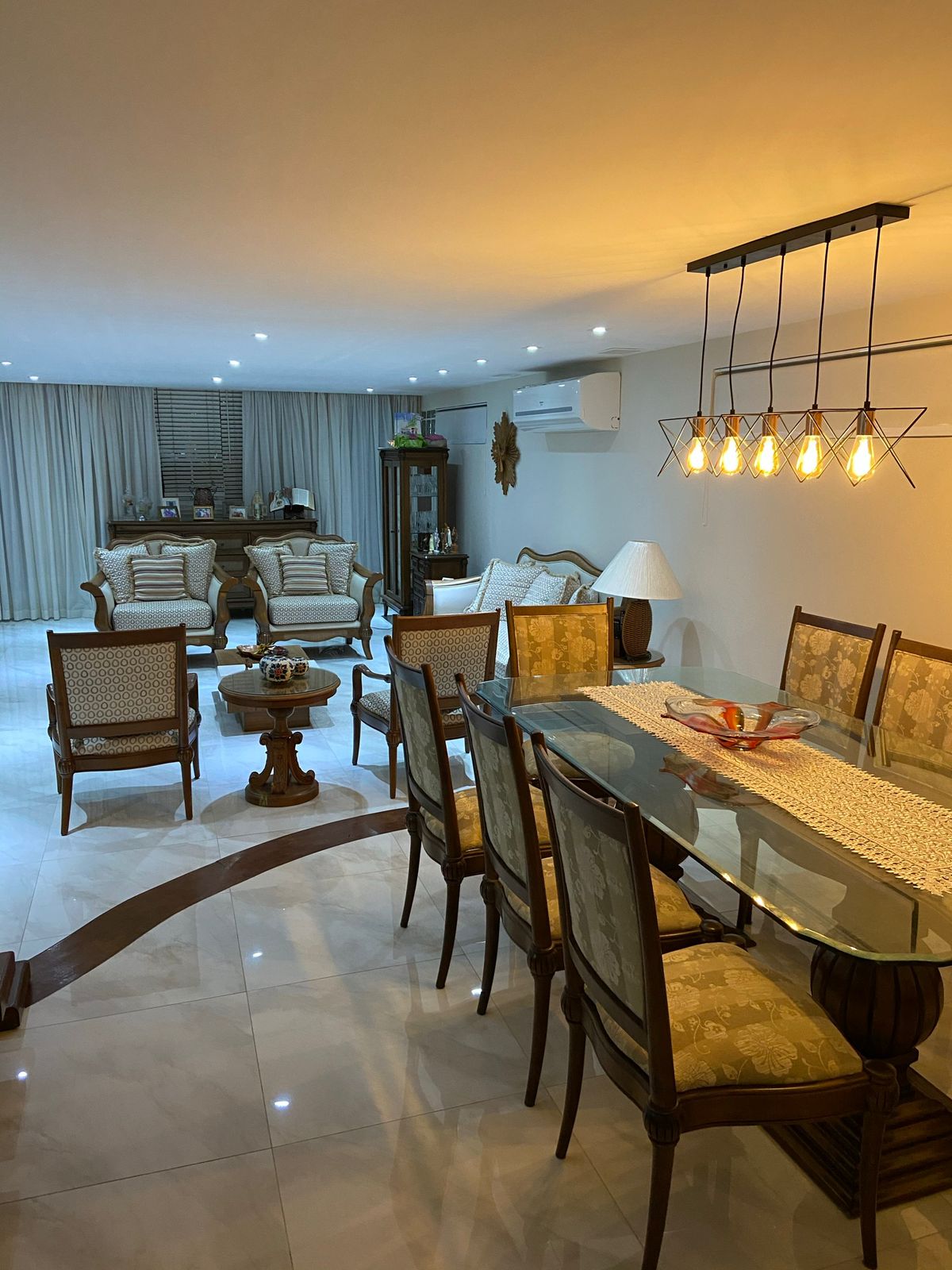 Sala de estar e jantar do apartamento na Lagoa, com mesa de vidro, cadeiras estofadas e lustre de pêndulos