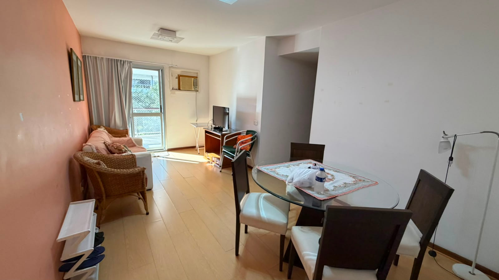 Sala de estar e jantar do apartamento no Condomínio Pablo Picasso, no Recreio dos Bandeirantes, Barra Bonita, com sofá, poltronas de vime, mesa de vidro e porta para a varanda