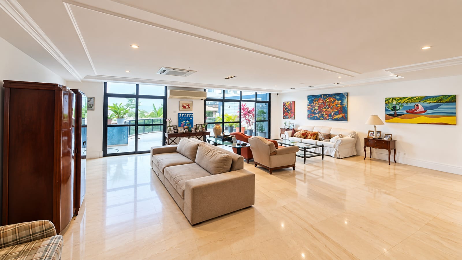 Sala de estar da cobertura duplex no Parque das Rosas, na Barra da Tijuca, com sofás, piso de mármore claro, quadros coloridos e porta de vidro para a varanda