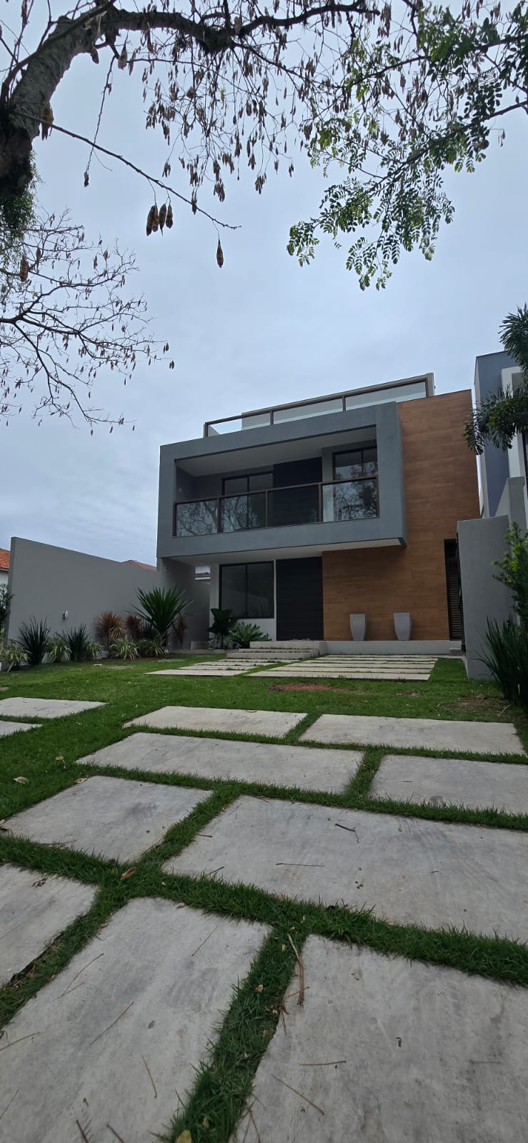 Fachada da casa dúplex de projeto moderno no Recreio, Vivendas do Sol, com dois andares, revestimento de madeira, vidros e jardim com caminho de placas de concreto