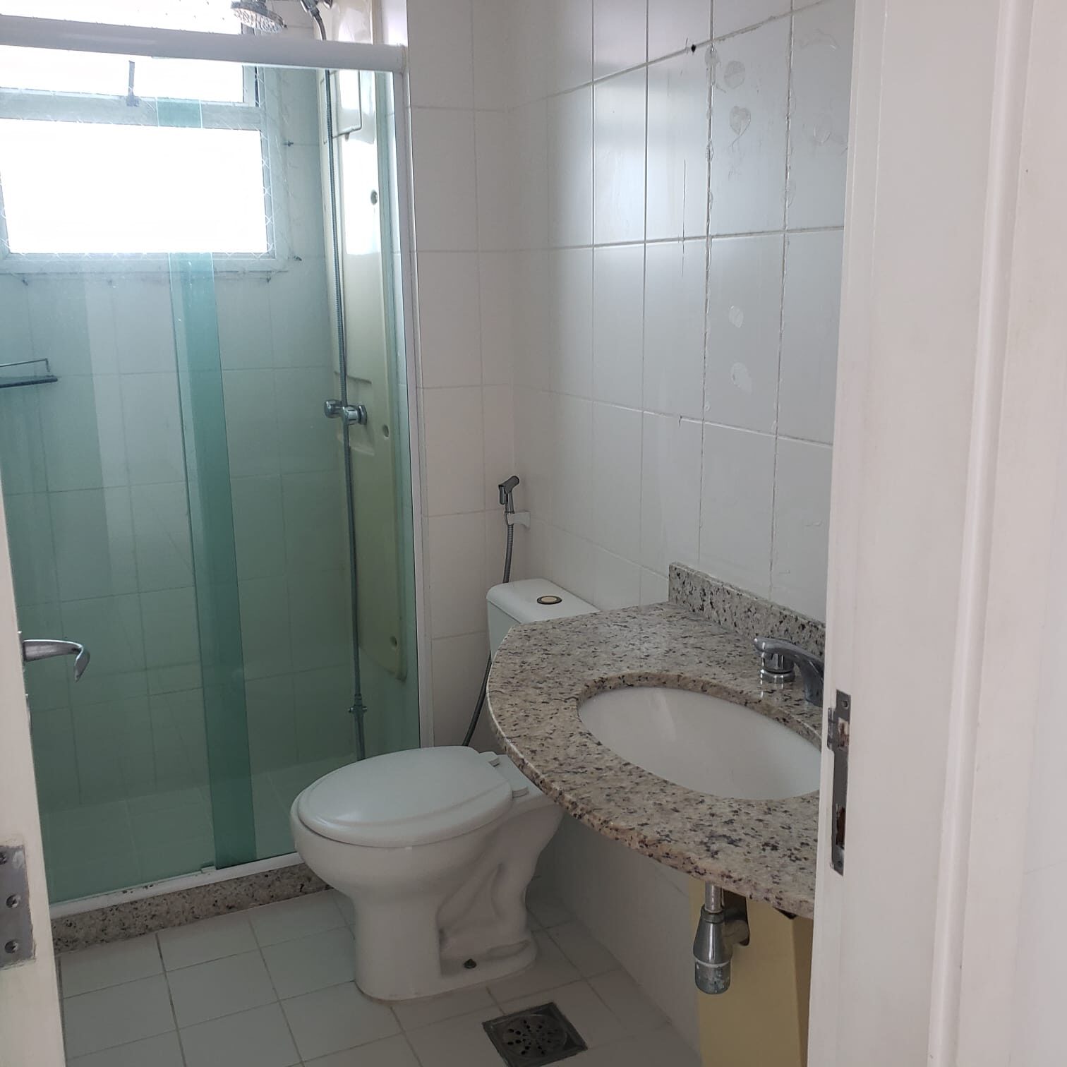 Banheiro do apartamento na Vila do Pan, com box de vidro verde, pia de granito e vaso sanitário