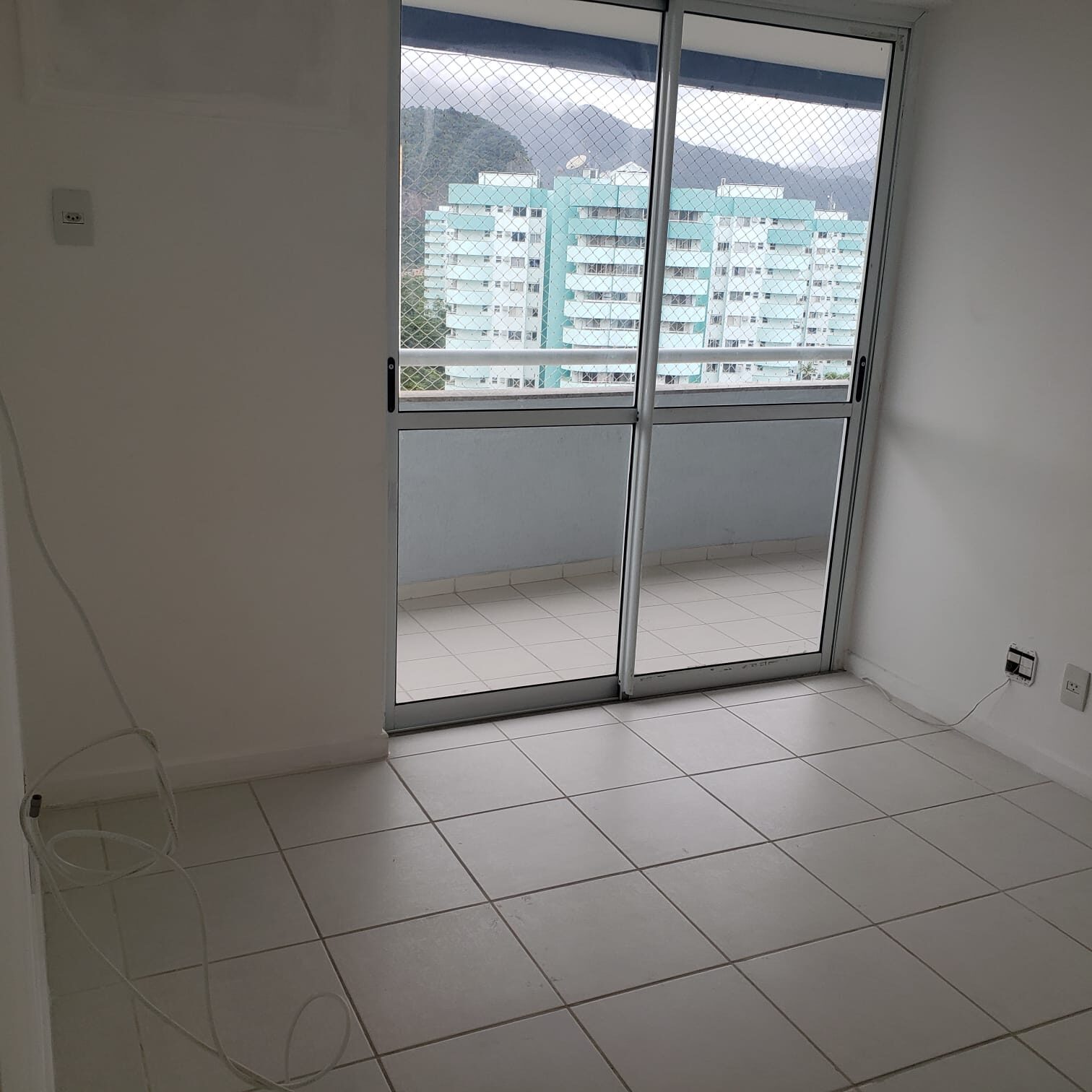 Sala do apartamento na Vila do Pan, com piso claro e porta de vidro de correr para a varanda