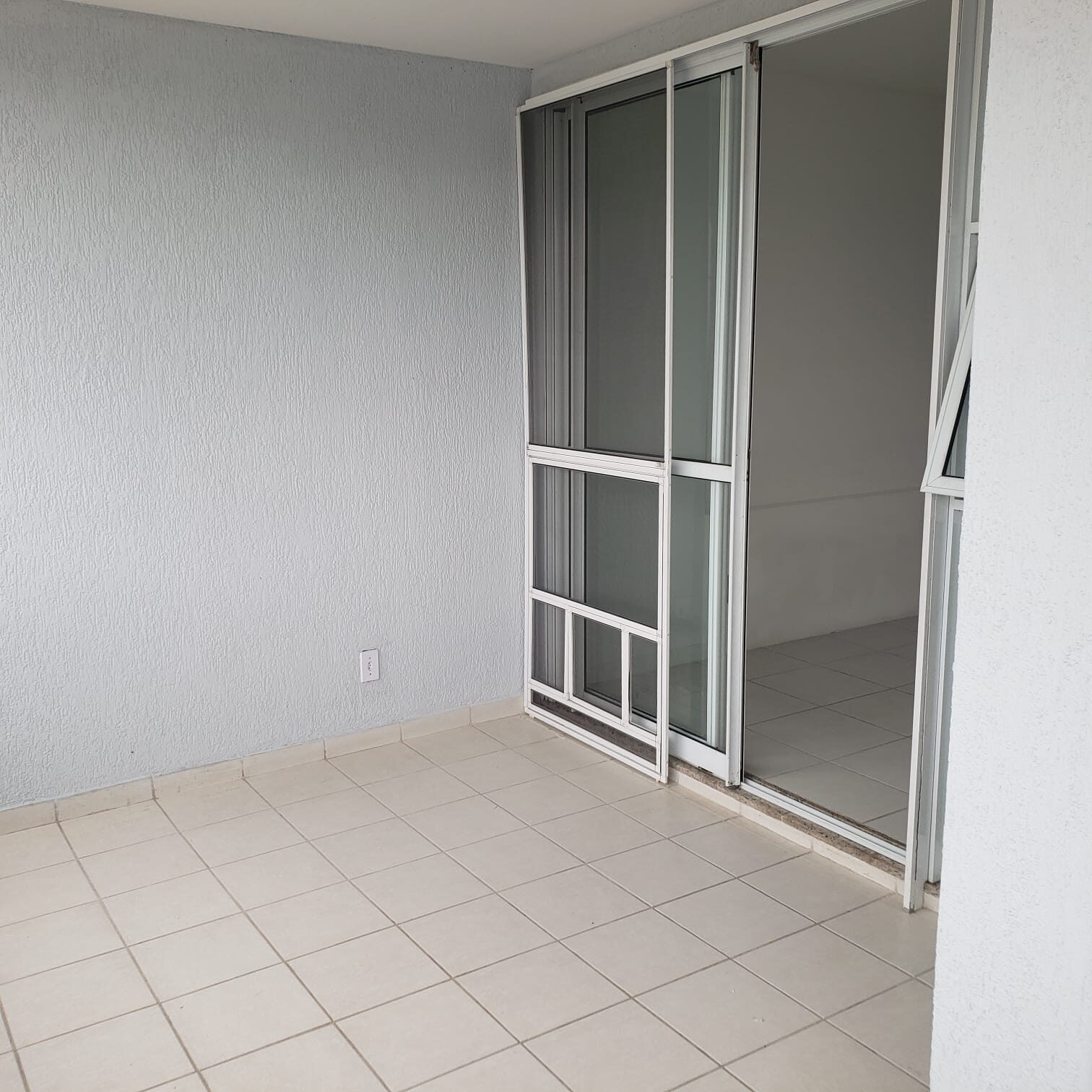 Varanda do apartamento na Vila do Pan, com piso claro e porta de correr de vidro